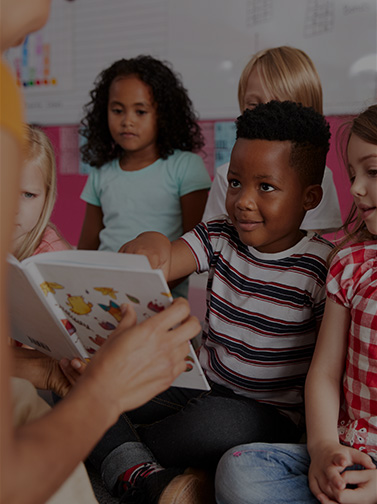 Group of children sitting on floor as adult reads from storybook.