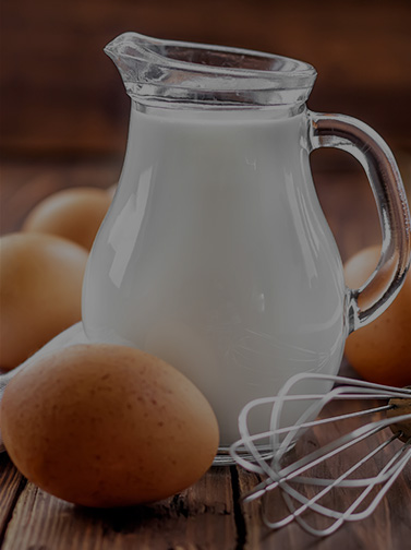 a pitcher of milk surrounded by brown eggs and a whisk