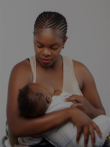 Woman breastfeeding infant wearing striped onesie.