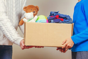 Person in blue sweater handing box full of clothing donations to person in white sweater.