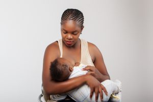 Woman breastfeeding infant wearing striped onesie.