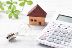 A lightbulb and a tiny house sitting on a table next to a calculator.