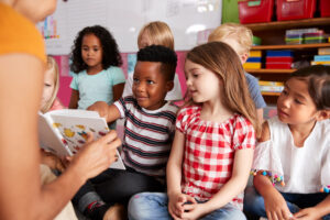 Group of children sitting on floor as adult reads from storybook.