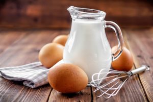 a pitcher of milk surrounded by brown eggs and a whisk