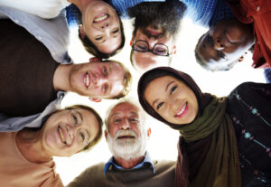 Multicultural group of people in huddle looking down at camera.