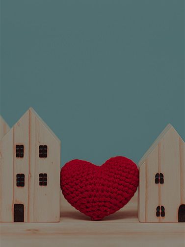 A crocheted heart nestled between tiny wooden houses.