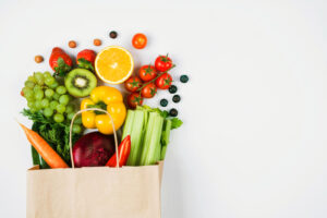 Paper bag spilling assorted fruits and vegetables onto a surface.