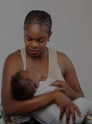 Woman breastfeeding infant wearing striped onesie.