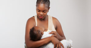 Woman breastfeeding infant wearing striped onesie.