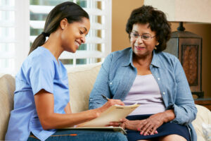 Medical professional writing on paper document while elderly woman looks on.