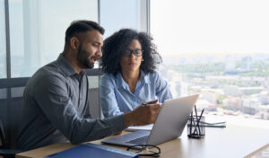 Male executive manager mentors young woman at desk with laptop.