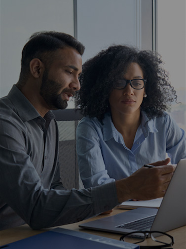 Male executive manager mentors young woman at desk with laptop.