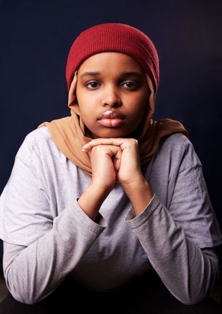 Girl wearing hijab resting her chin on clasped hands.