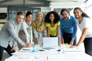 Multicultural group of professionals gathered around meeting table with notes and laptop.