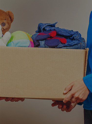 Person in blue sweater handing box full of clothing donations to person in white sweater.