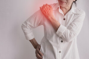 Elderly woman clutching her shoulder in pain.