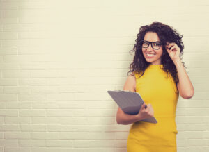 Young woman wearing glasses holding clipboard.