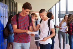 Two male students standing in hallway and looking at documents.