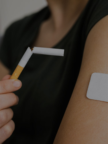 Closeup of woman holding broken cigarette next to arm with patch.
