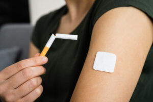 Closeup of woman holding broken cigarette next to arm with patch.