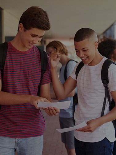 Two male students standing in hallway and looking at documents.