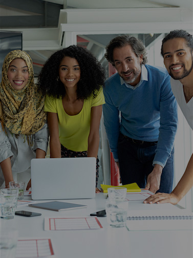 Multicultural group of professionals gathered around meeting table with notes and laptop.